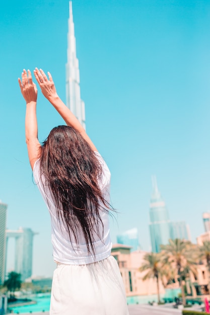 Mujer feliz caminando en Dubai con rascacielos en el fondo. Vista desde atrás.