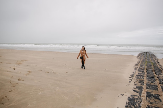 Mujer feliz caminando en la playa a lo largo del mar del norte afuera es frío y lluvioso