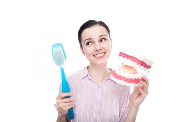 mujer feliz con una camisa morada sosteniendo un enorme cepillo de dientes en la mano una enorme maqueta de mandíbula