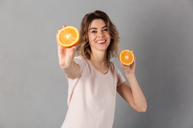 Mujer feliz en camiseta mostrando naranjas y sobre gris