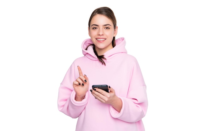 Mujer feliz con capucha rosa apuntando con el dedo hacia arriba sosteniendo el teléfono móvil aislado en el espacio de copia en blanco, publicidad.