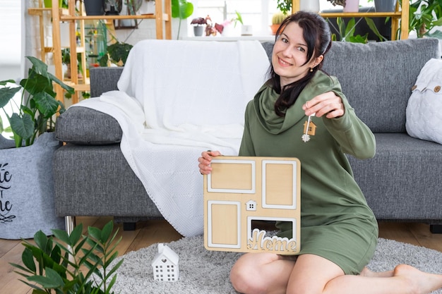 Mujer feliz en casa sostiene en las manos el marco de fotos con figura en la plantilla de casa y llave en el interior Proyecto de casa de ensueño compra de bienes raíces seguro hipoteca reserva de alquiler