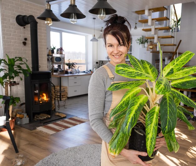Una mujer feliz en una casa verde con una maceta en las manos sonríe y cuida una flor El interior de una acogedora casa ecológica una estufa de chimenea un pasatiempo para cultivar y criar plantas caseras