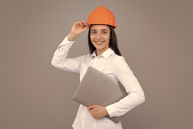 Mujer feliz con casco protector con computadora portátil aislada en fondo gris Arquitecto