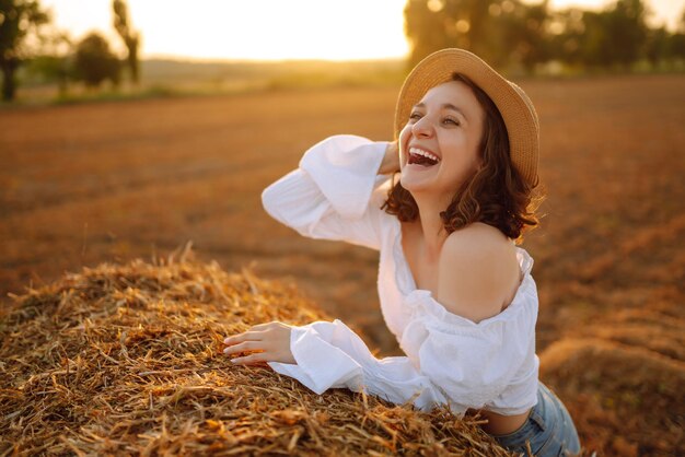 Foto mujer feliz cerca del pajar al atardecer concepto de moda vacaciones en la naturaleza relajación y estilo de vida