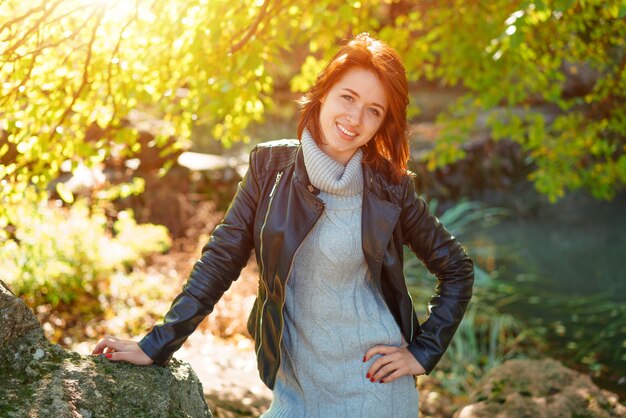 Mujer feliz en una chaqueta de cuero en un parque cerca de un árbol sonriendo