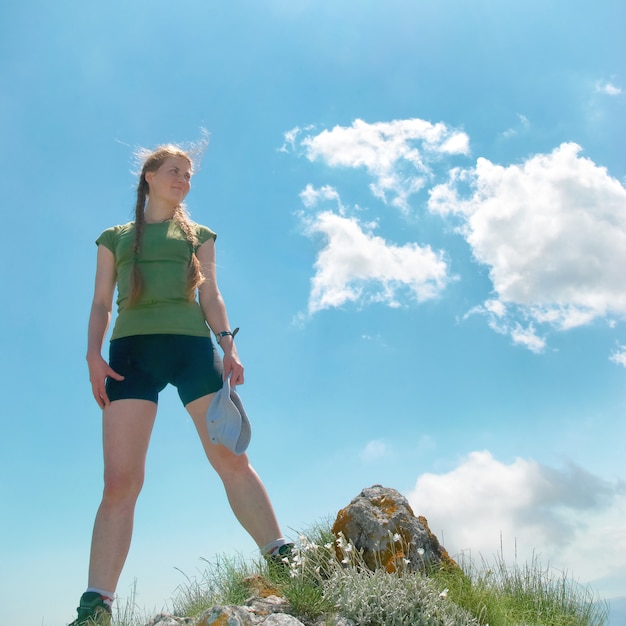 Mujer feliz en la cima de una montaña con cielo azul y nubes