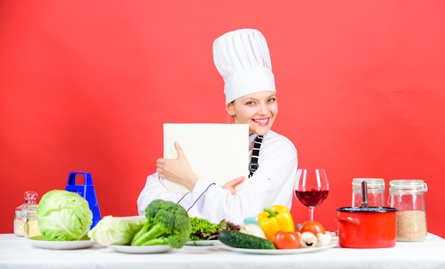 Mujer feliz cocinando comida saludable por receta menú de cafetería Mujer a dieta con sombrero de cocinero chef profesional sobre fondo rojo alimentación orgánica y vegetariana