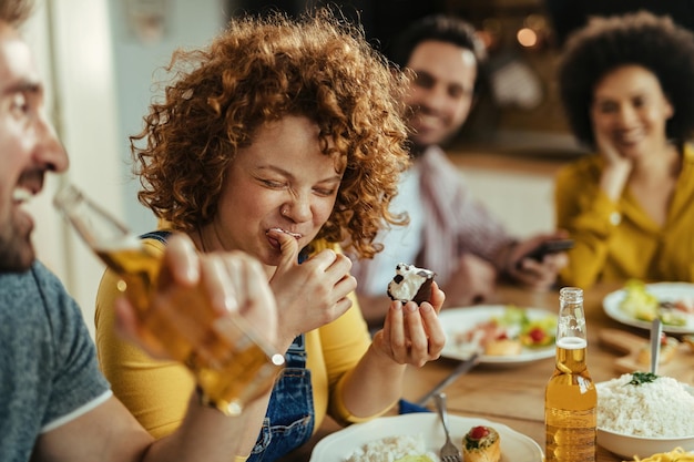 Mujer feliz comiendo postre y divirtiéndose con sus amigos después del almuerzo en el comedor