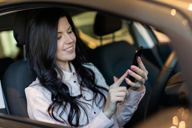 Mujer feliz comprador examina su nuevo vehículo en concesionario de automóviles