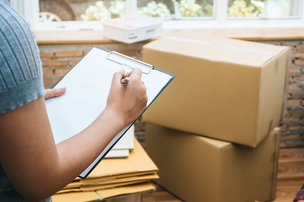 Mujer feliz comprobando cosas en caja de cartón antes de enviar a la empresa de transporte y movi