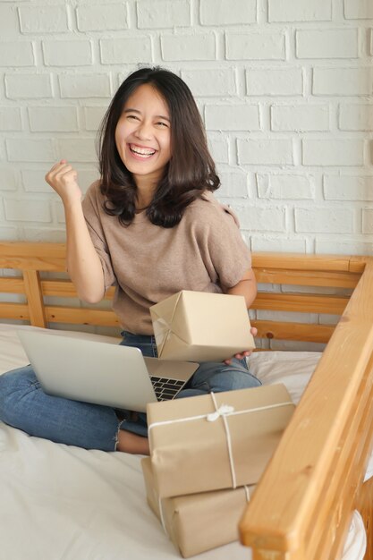 Mujer feliz con computadora y caja de paquete de productos en casa, trabajo en casa, concepto de entrega de mercancías