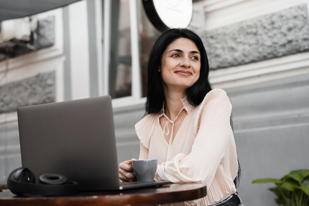 Mujer feliz con computadora portátil y café en las manos disfruta de la vida Manos con pigmentación de la piel vitíligo Estilo de vida con enfermedad estacional de la piel Trabajando en la computadora portátil en la cafetería