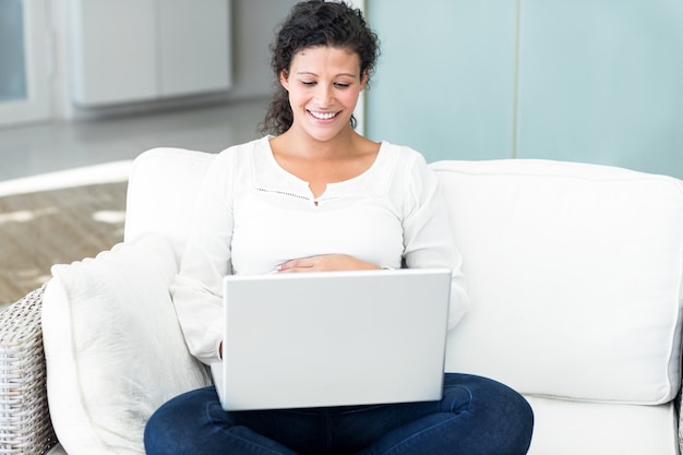 Mujer feliz con la computadora portátil en el sofá