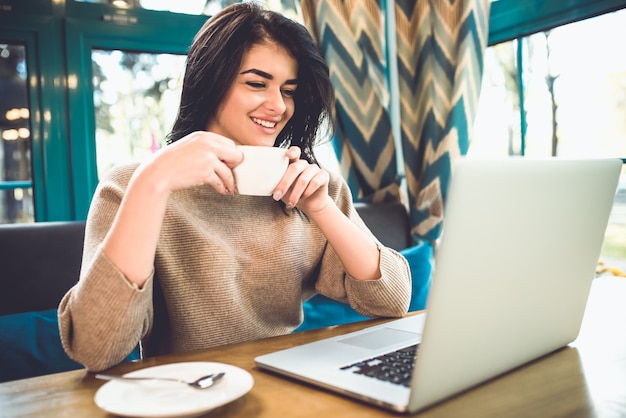 La mujer feliz con una computadora portátil tomar un café en la cafetería