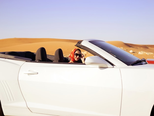 Mujer feliz conduce por la carretera del desierto en coche convertible