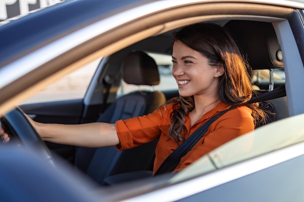 Mujer feliz conduciendo un coche y sonriendo Lindo joven éxito feliz mujer morena está conduciendo un coche Retrato de una conductora feliz conduciendo un coche con cinturón de seguridad