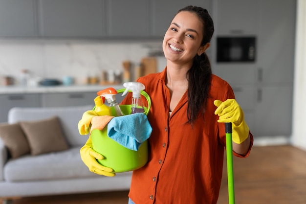 Mujer feliz con un cubo de productos de limpieza y un trapeador