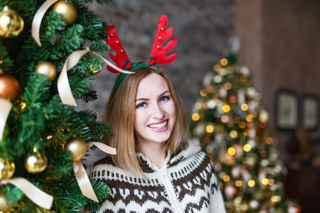 Mujer feliz con cuernos de Navidad de un ciervo cerca del árbol de Navidad