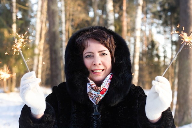 La mujer feliz en el cuerpo en la naturaleza en invierno con bengalas, Navidad