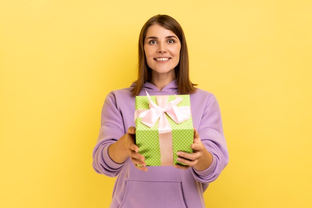 Mujer feliz dando caja azul a la cámara y sonriendo compartiendo regalo de vacaciones felicitando por cumpleaños