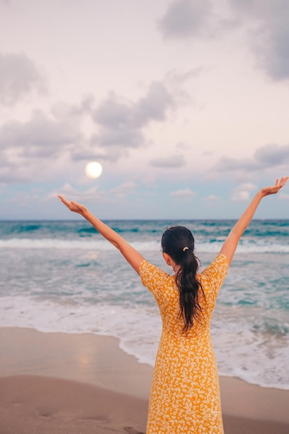 Mujer feliz disfrutando de la hermosa puesta de sol con una gran luna llena en la playa