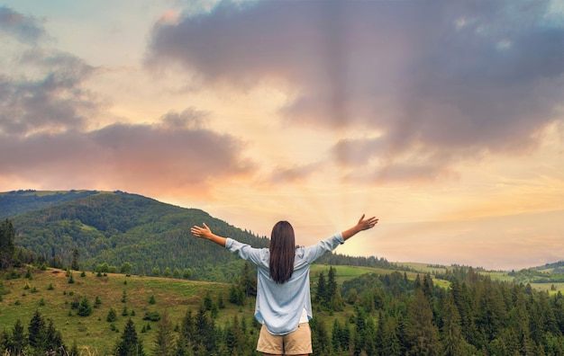 Mujer feliz disfrutando de la puesta de sol mientras está de pie en la cima de la montaña