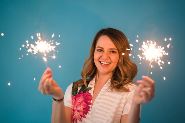 Mujer feliz divirtiéndose con una bengala sobre fondo azul con copyspace.