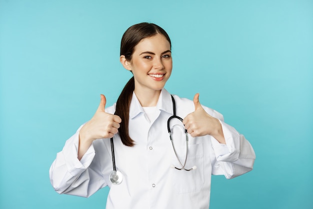 Mujer feliz doctora trabajadora médica en bata blanca mostrando los pulgares hacia arriba en aprobación como algo elogioso...