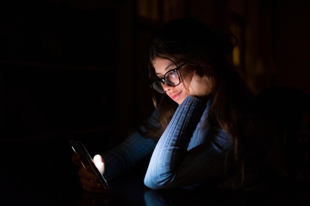 Una mujer feliz e imnsónica que usa el teléfono a altas horas de la noche en el dormitorio de su casa charlando Chica en línea navegando por la red revisando las redes sociales Concepto de tecnología usando Internet