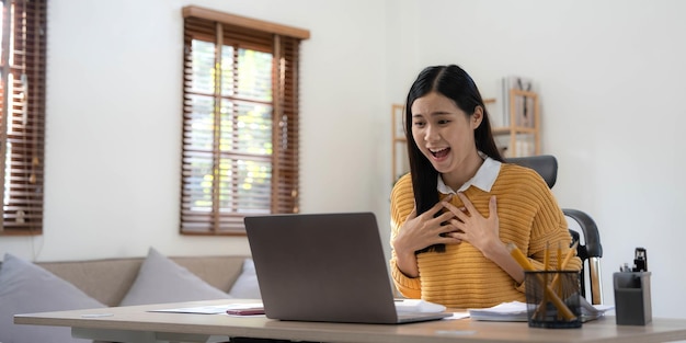 Mujer feliz y emocionada mirando la pantalla de la computadora portátil celebrando una victoria en línea feliz joven asiática gritando de alegría en casa