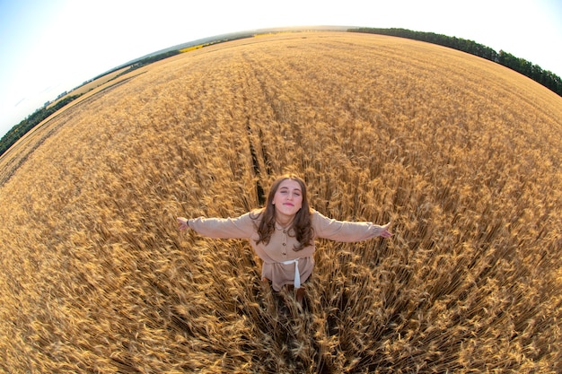 Mujer feliz se encuentra en un campo de trigo en el verano con el telón de fondo de una puesta de sol