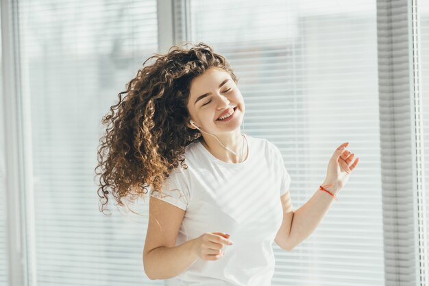 La mujer feliz escuchando música cerca de la ventana.