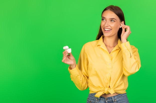 Mujer feliz escuchando música en línea poniendo auriculares fondo verde