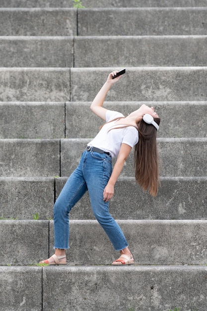 Mujer feliz escuchando música en su teléfono y bailando sola en las escaleras de una tribuna.