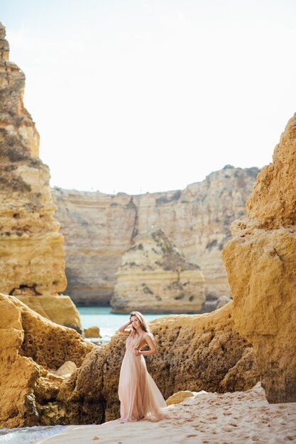 mujer feliz con la espalda en un vestido amarillo de pie en la playa y el mar al atardecer