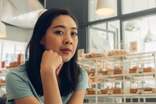 La mujer feliz está sentada y espera a alguien en el café de la panadería.