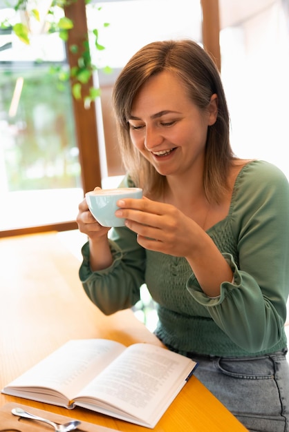 Una mujer feliz está tomando café y leyendo su libro favorito en un café.