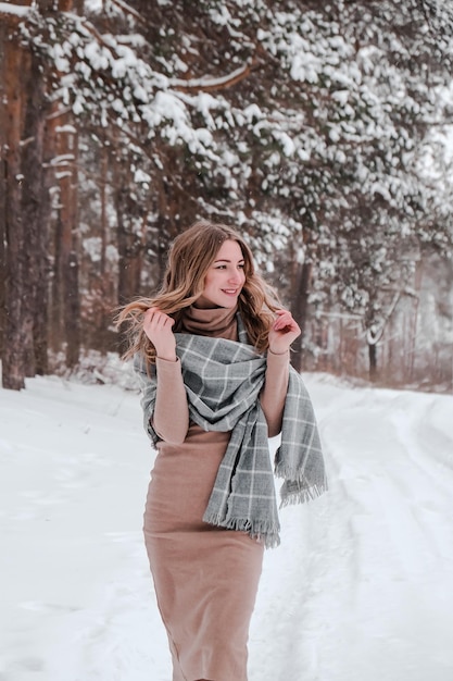 Mujer feliz en el fondo del bosque de invierno. Chica guapa joven en el bosque al aire libre. Retrato de una bella mujer alegre. Moda de invierno. vestido con bufanda
