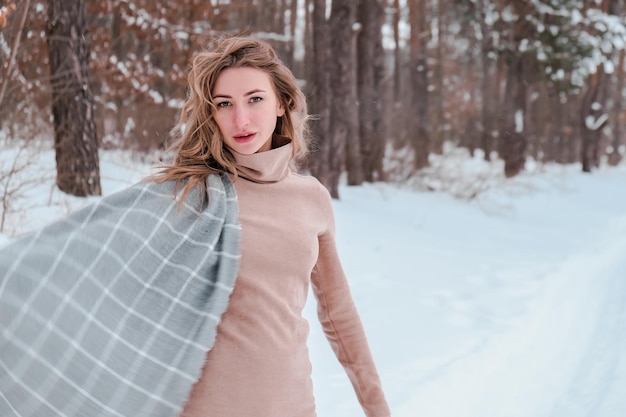 Mujer feliz en el fondo del bosque de invierno. Chica guapa joven en el bosque al aire libre. Retrato de una bella mujer alegre. Moda de invierno. vestido con bufanda