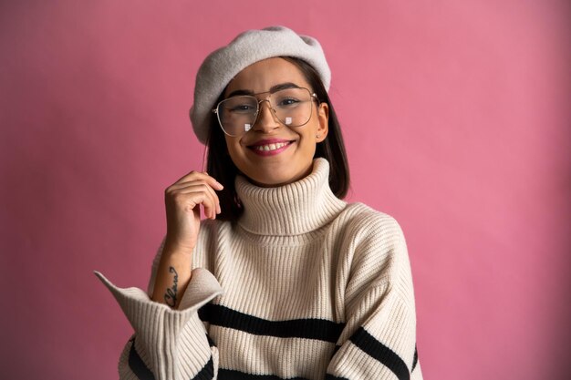 Foto una mujer feliz con gafas y una boina está sonriendo y usando gafas sobre un fondo rosa