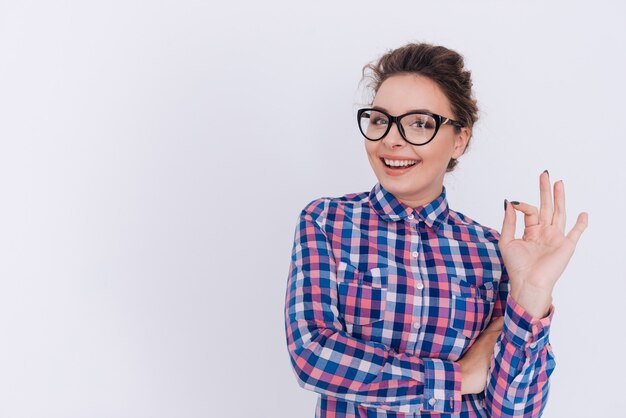 Mujer feliz en gafas y camisa a cuadros mostrando signo ok