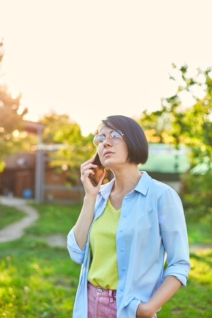 Mujer feliz con gafas hablando por teléfono móvil al aire libre