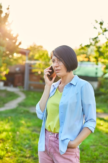 Mujer feliz con gafas hablando por teléfono móvil al aire libre