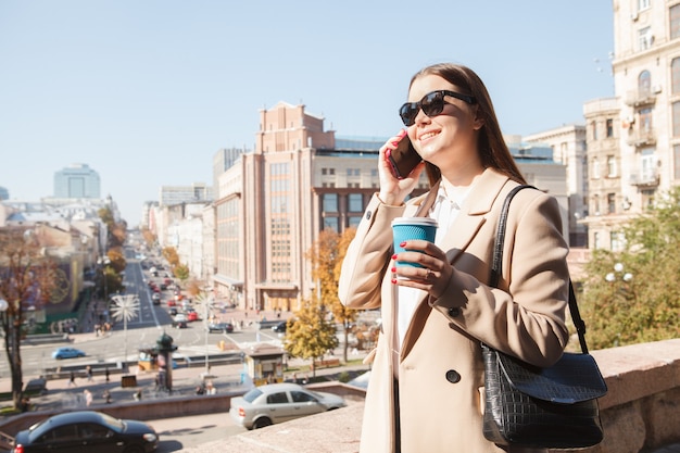 Mujer feliz con gafas de sol, hablando por teléfono en el centro de la ciudad