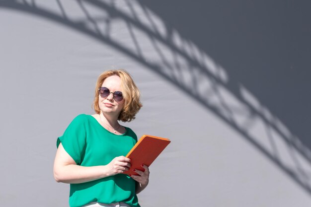 Mujer feliz con gafas de sol navegando por la tableta apoyándose en la pared en la calle hermosa sombra