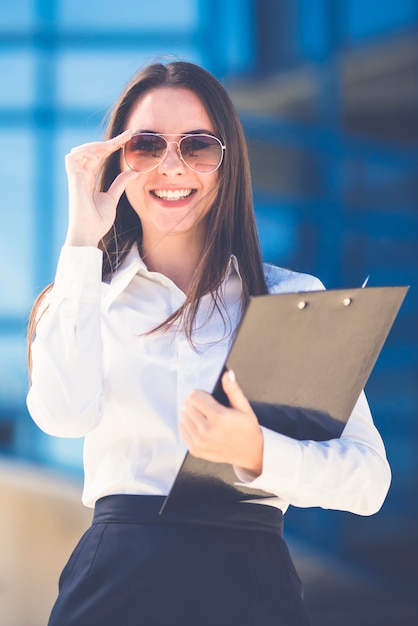 La mujer feliz en gafas de sol de pie con una tableta