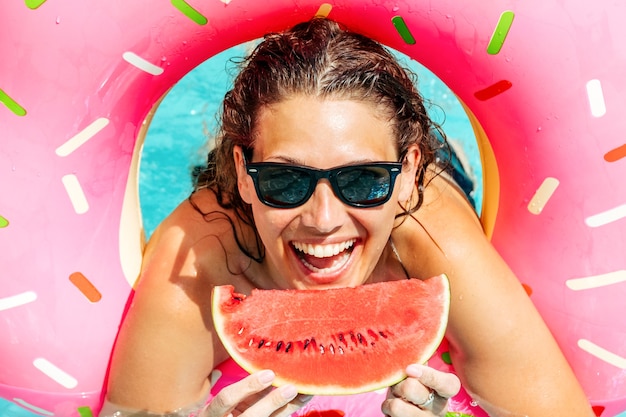 Mujer feliz con gafas de sol con sandía roja disfrutar en la piscina con anillo de goma rosa