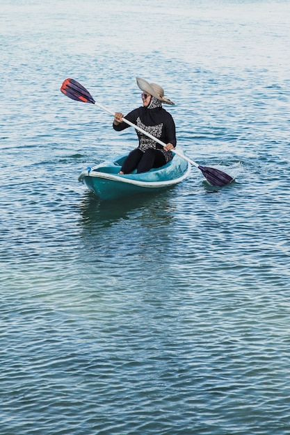 Mujer feliz con gafas de sol y sombrero de verano remando un kayak o un bote pequeño en el océano en la isla Karimun Jawa