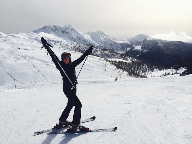 Mujer feliz gestando mientras esquía en un campo nevado por las montañas contra el cielo